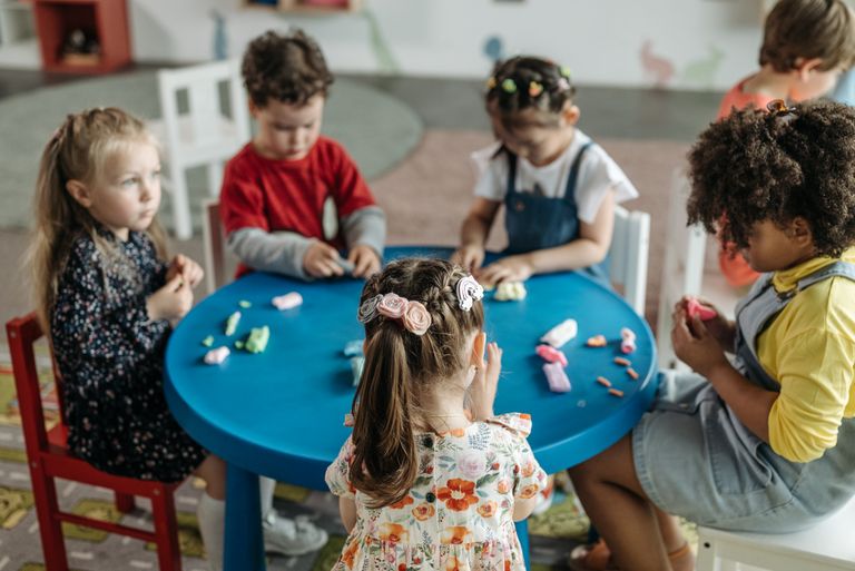Group of preschool children playing with clay at a colorful table in a classroom.
